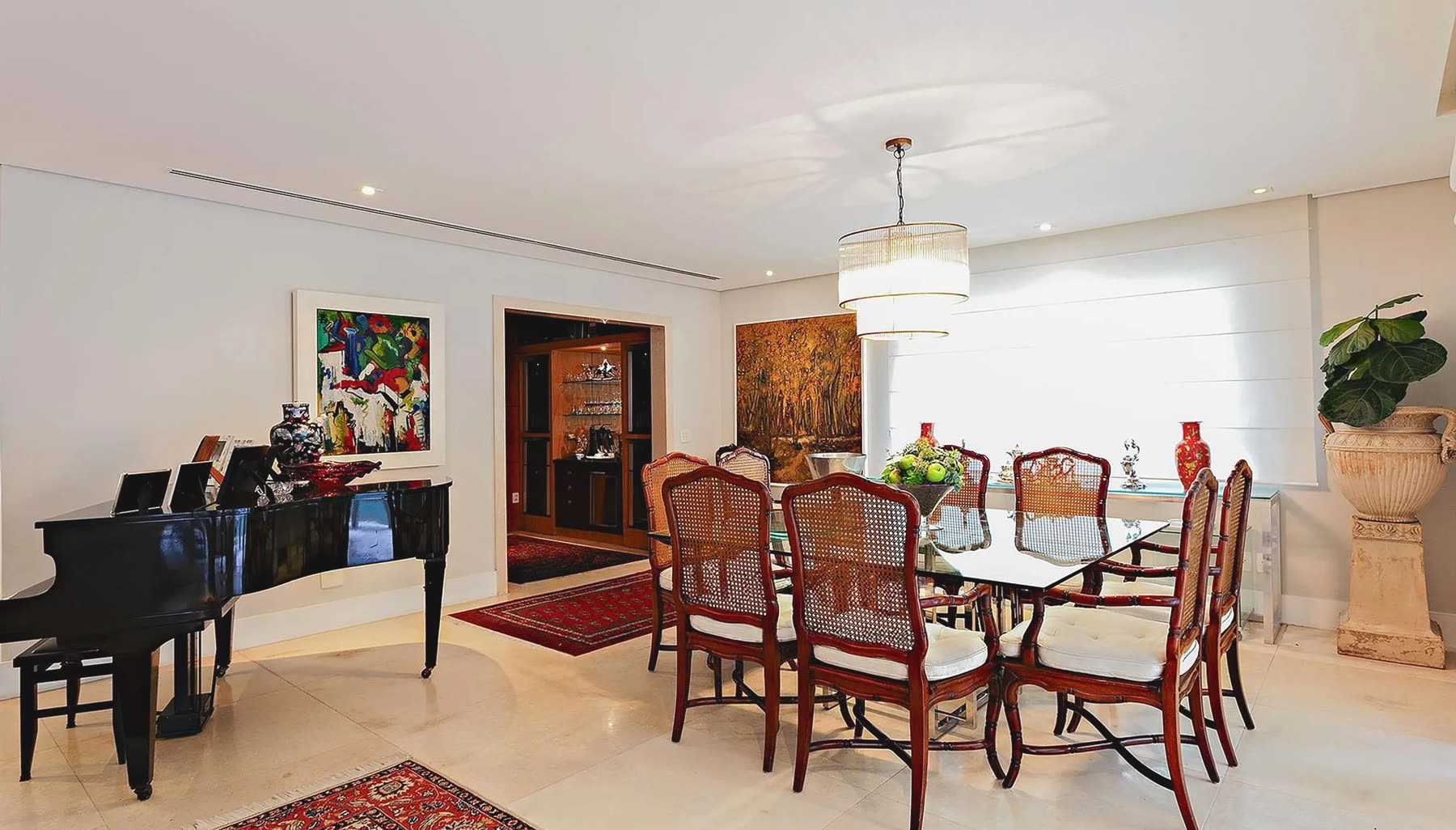 Sala de jantar com mesa de vidro, cadeiras de palhinha, lustre e piano ao lado